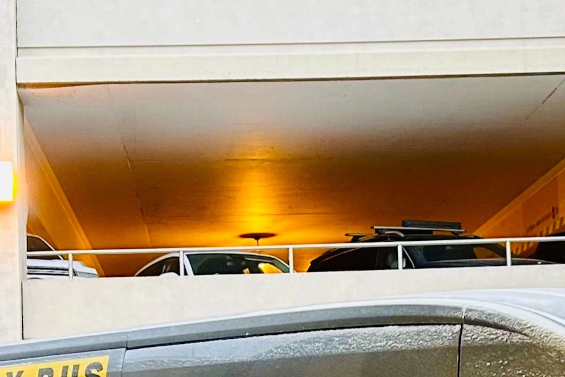 A black passenger van labeled "The Fairy Bus" parked in a multi-story garage near a yellow pillar with the number 15.