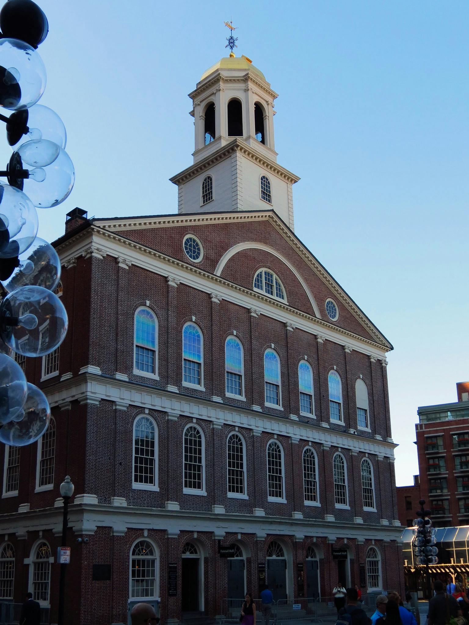 澄んだ青い空に面した、アーチ型の窓と金色のドームタワーを備えた歴史的なレンガ造りの建物。 人々は目の前を歩きます。