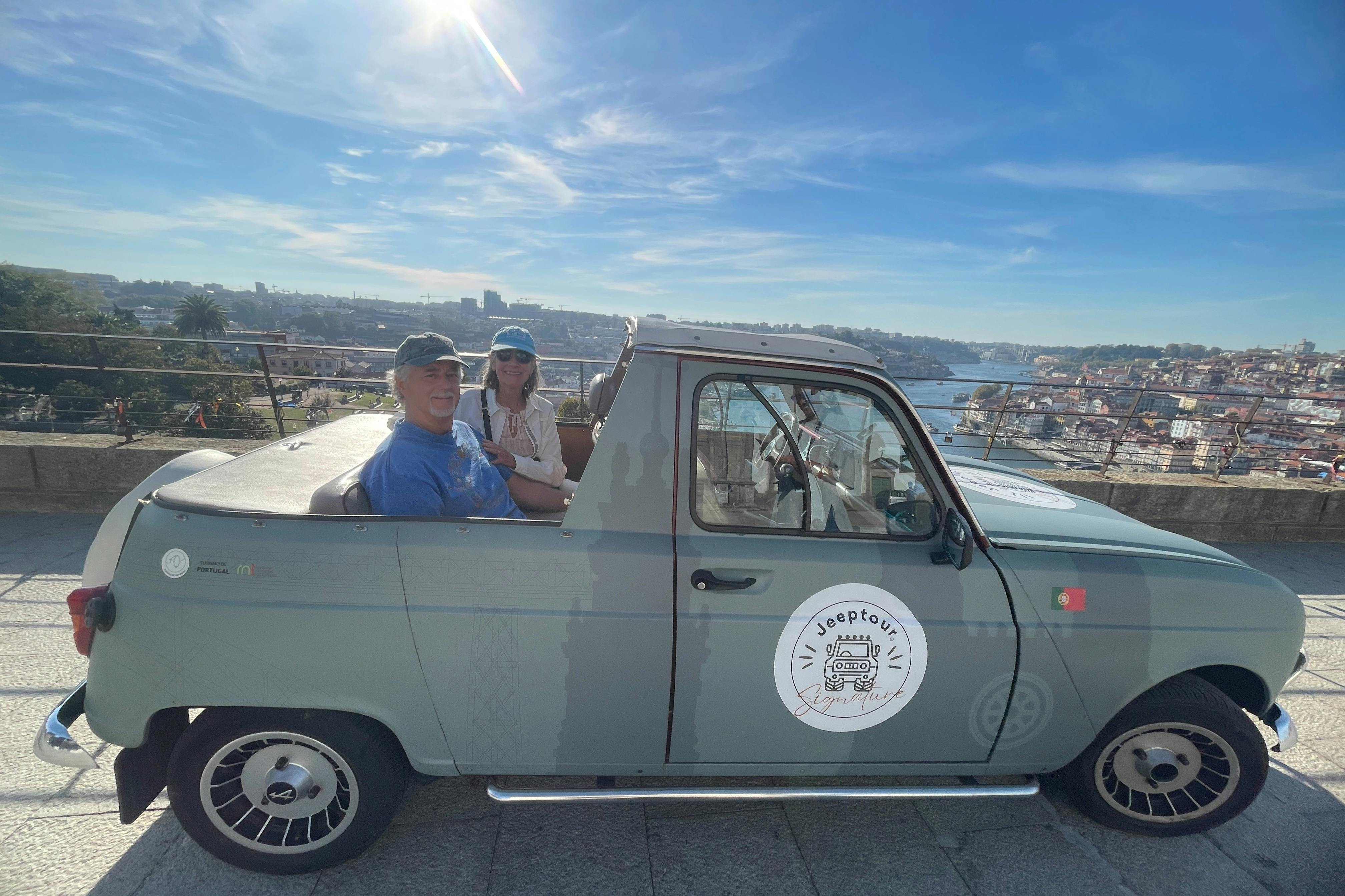 Two people sitting in a vintage convertible jeep with a sunlit cityscape in the background on a clear day.