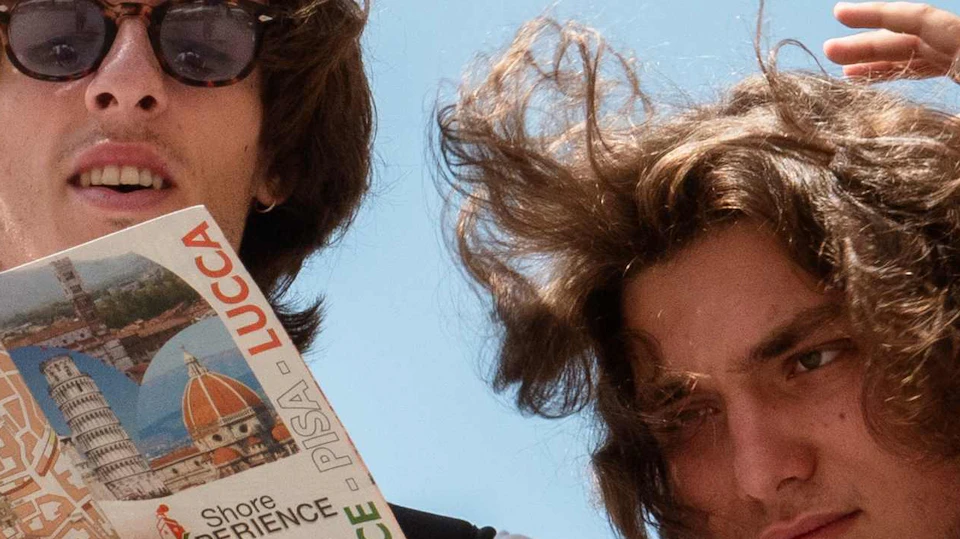 Two people outdoors, one wearing sunglasses and holding a map, both looking around under a clear blue sky.