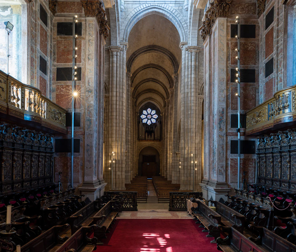 Interior of a large cathedral with high arches, ornate columns, wooden pews, red carpet, and a circular stained glass window.