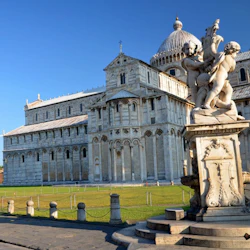 En historisk katedral med en skulptur av änglar i förgrunden, mot en klarblå himmel.