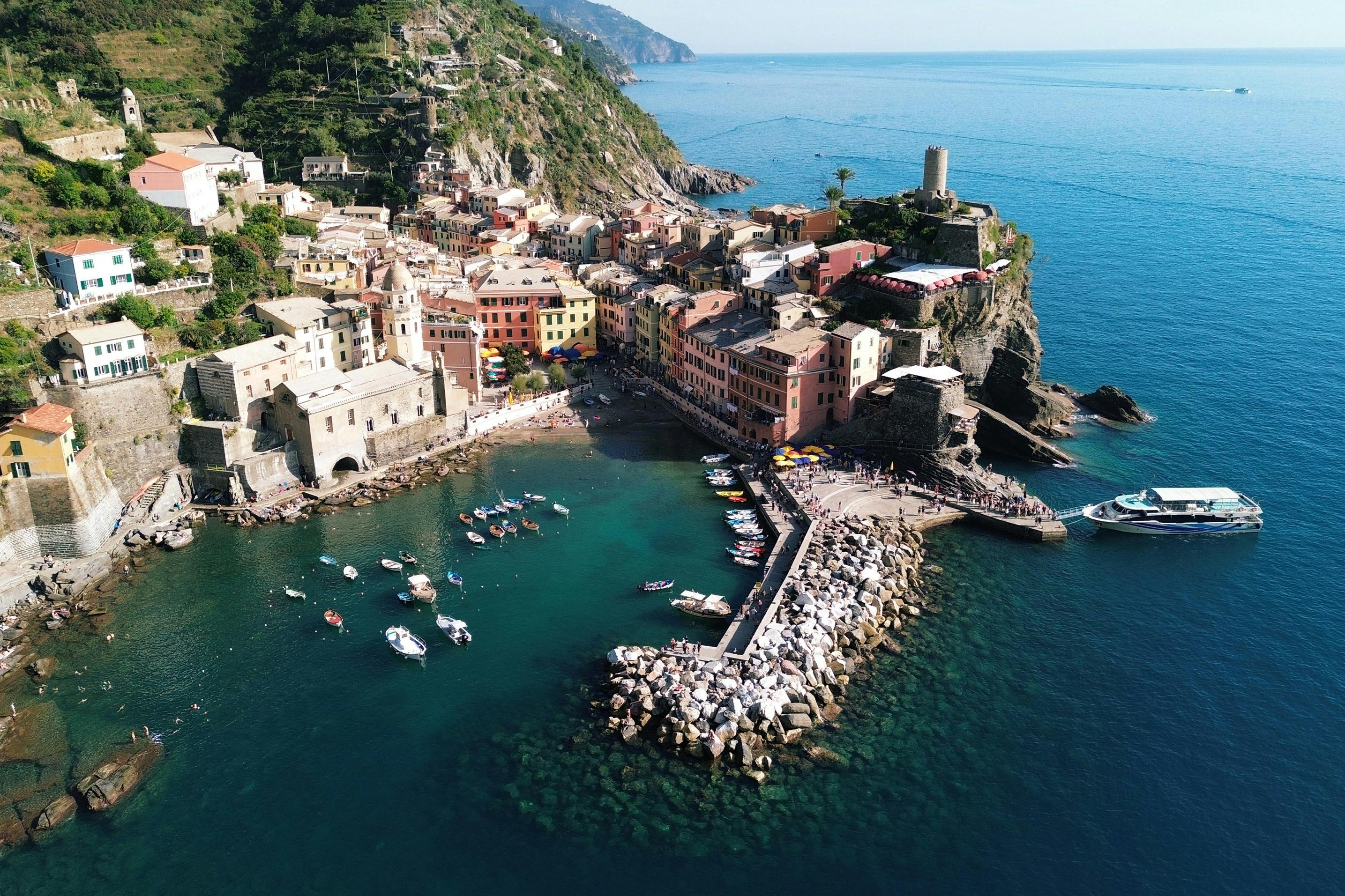 A coastal village with colorful buildings, a dock with boats, and a rocky shoreline surrounded by blue water and hills.