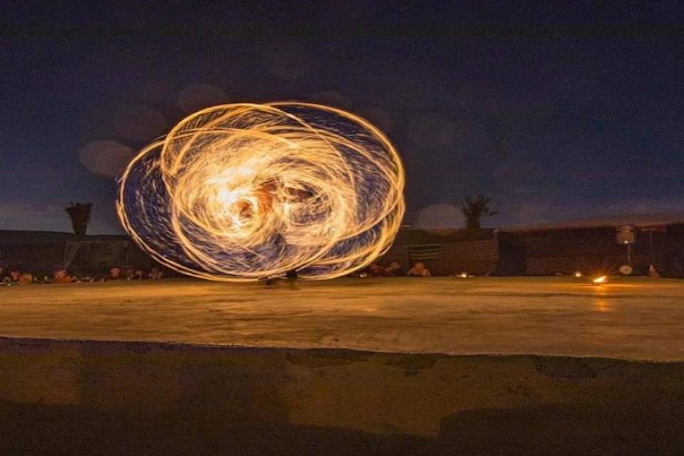 A performer spins multiple fire poi, creating swirling light patterns against a dark outdoor backdrop.