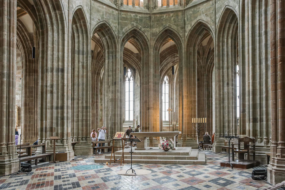 People inside a large, ornate cathedral with tall arched columns, stained glass windows, and a central altar.
