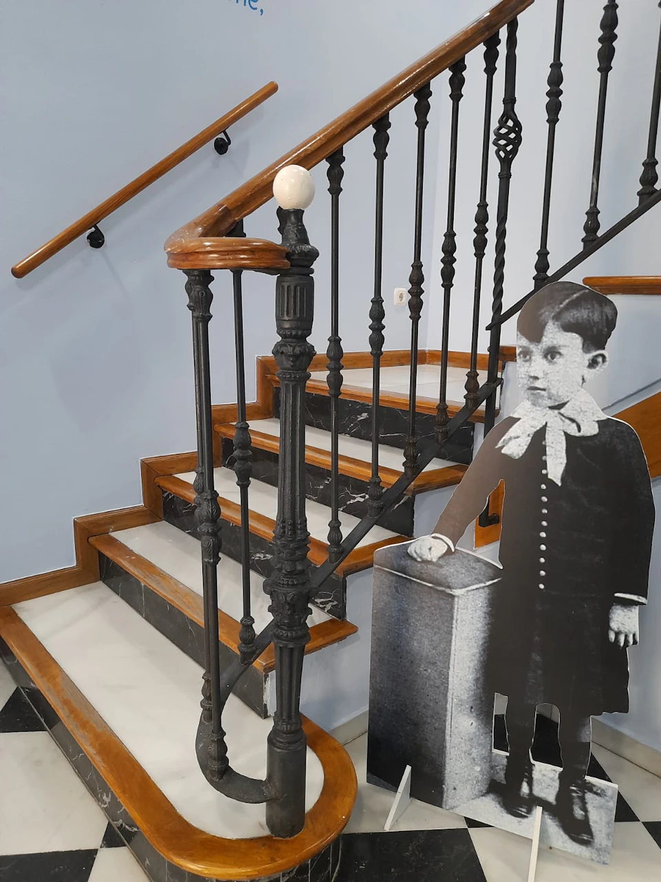 A staircase with wooden handrails and black metal balusters. A black-and-white cutout of a young boy stands beside the stairs.