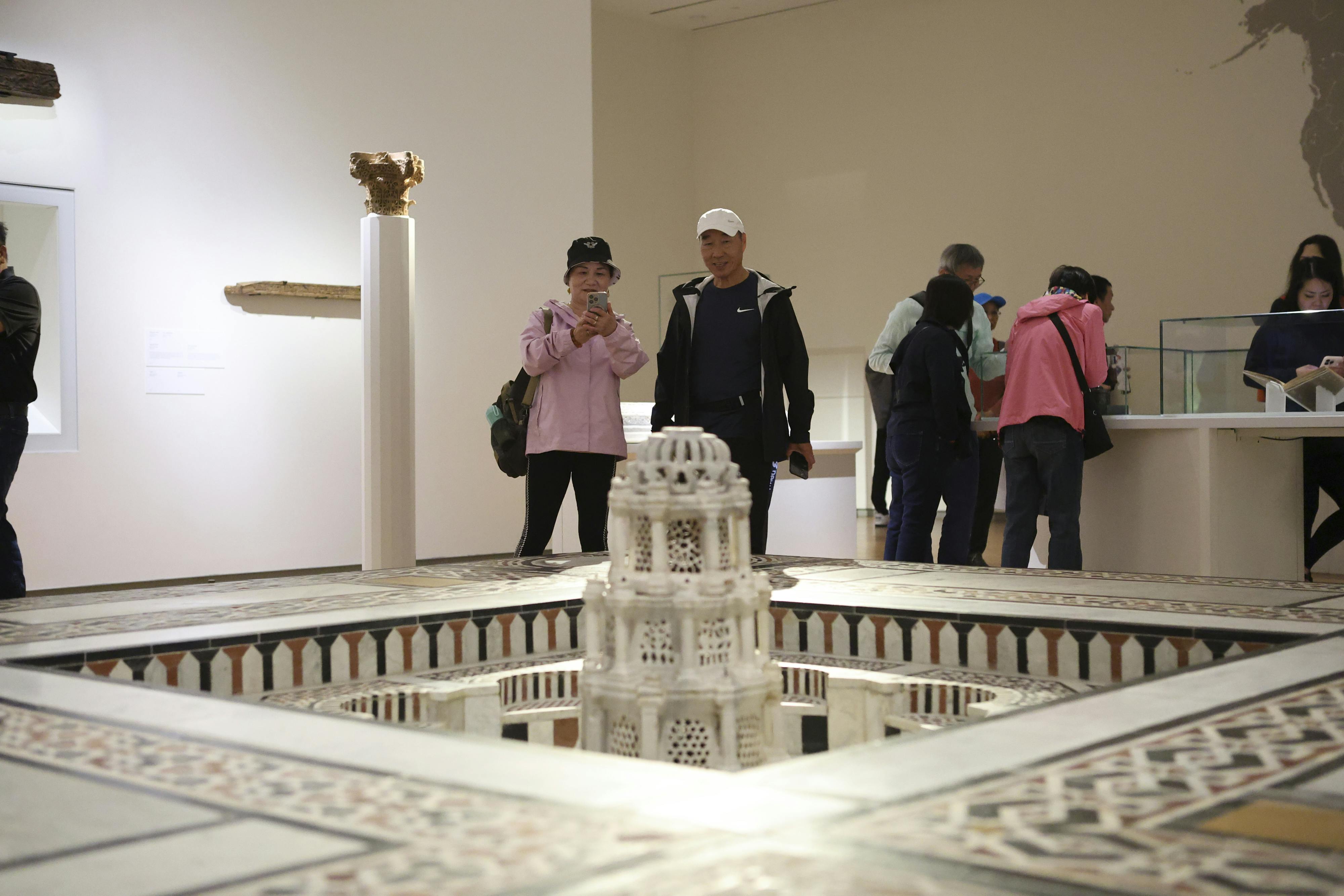 Lidé pozorují miniaturní architektonický model v muzejní expozici. Další artefakty jsou zobrazeny na podstavcích v pozadí.