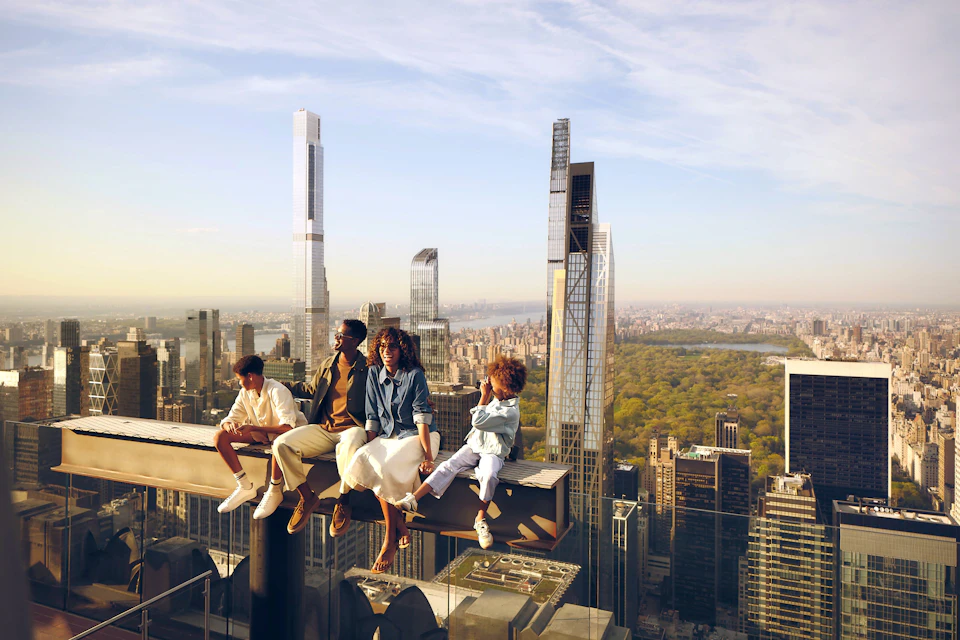 Four people sitting on a steel beam high above a cityscape with skyscrapers and a park visible in the background.