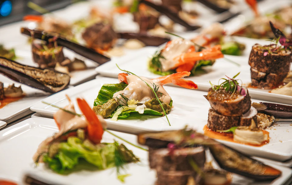 Plates of gourmet appetizers with shrimp, greens, and garnish, arranged neatly on a table.