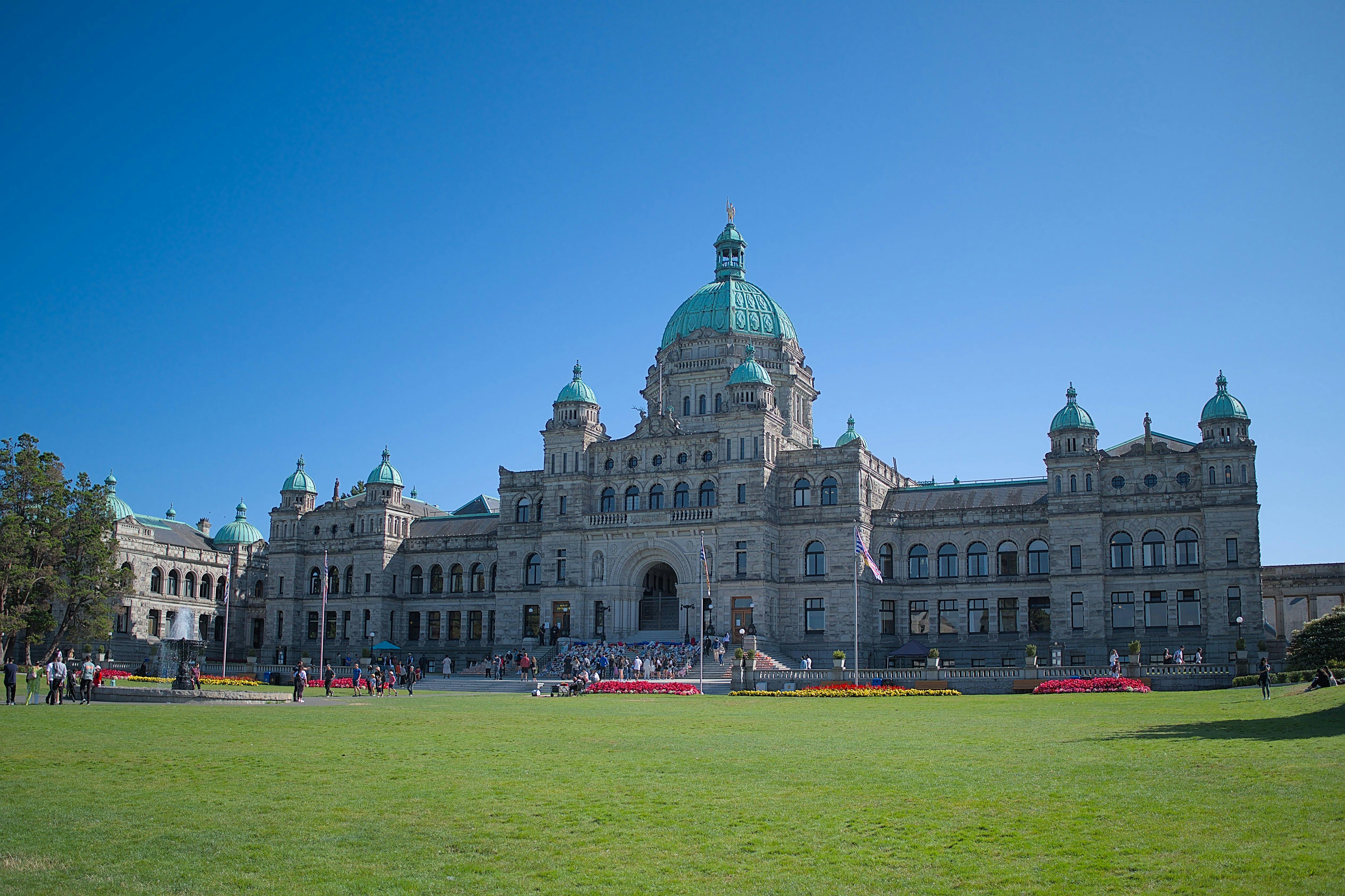 Ένα μεγάλο, ιστορικό κτίριο με πράσινους θόλους και συμμετρική πρόσοψη. Οι άνθρωποι συγκεντρώνονται στα σκαλιά και ένα πράσινο γρασίδι βρίσκεται σε πρώτο πλάνο.