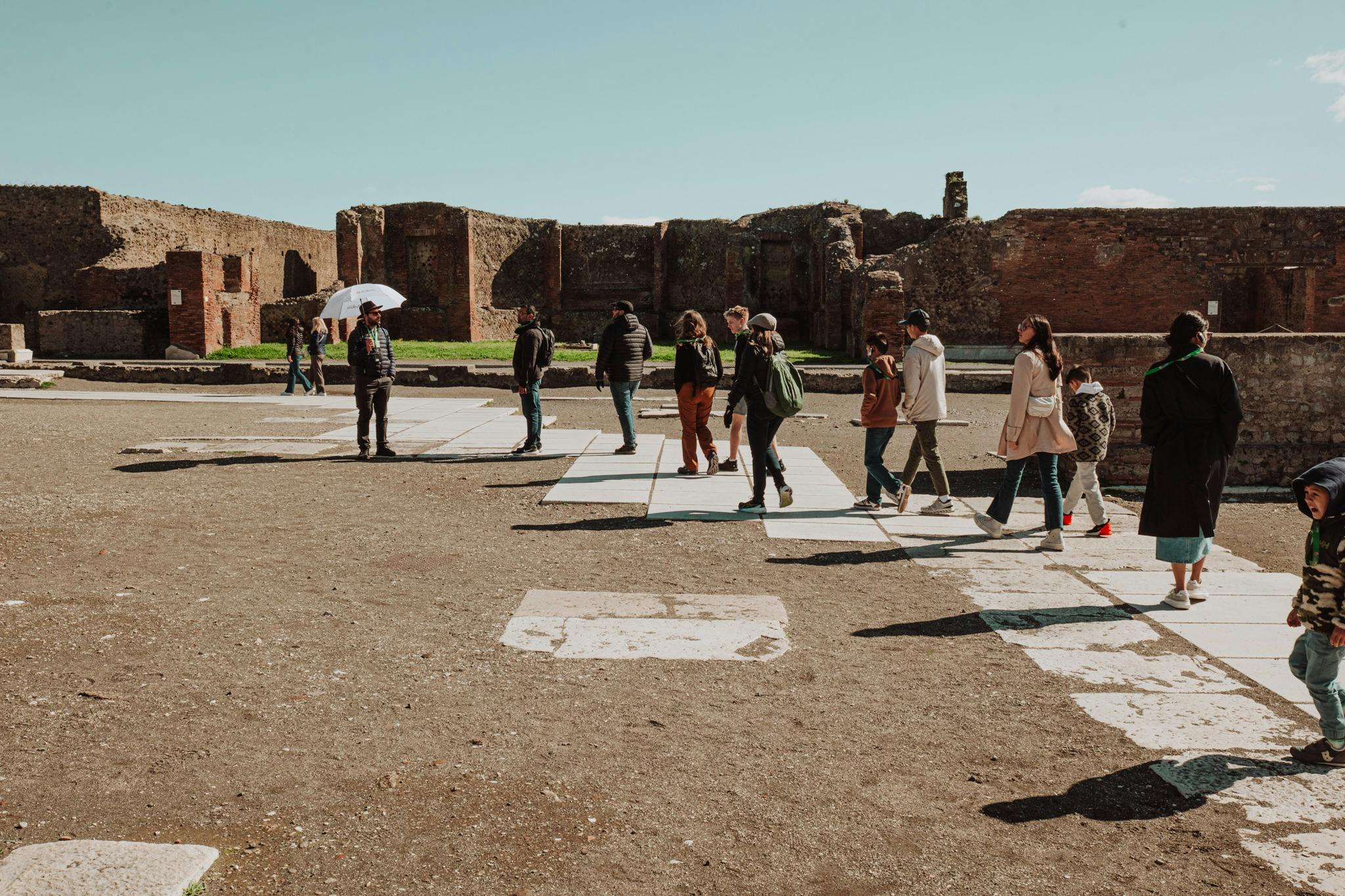 A group of people walking through a historic site with ancient brick ruins under a clear blue sky.