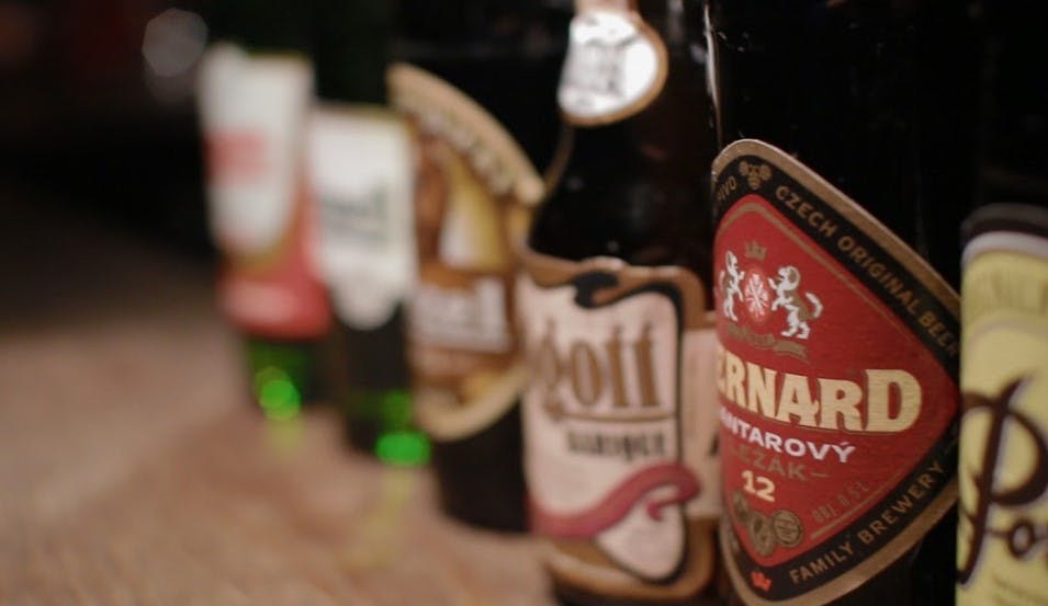 다양한 브랜드와 디자인을 보여주는 라벨이 있는 목재 표면에 여러 개의 맥주병이 줄지어 있습니다.