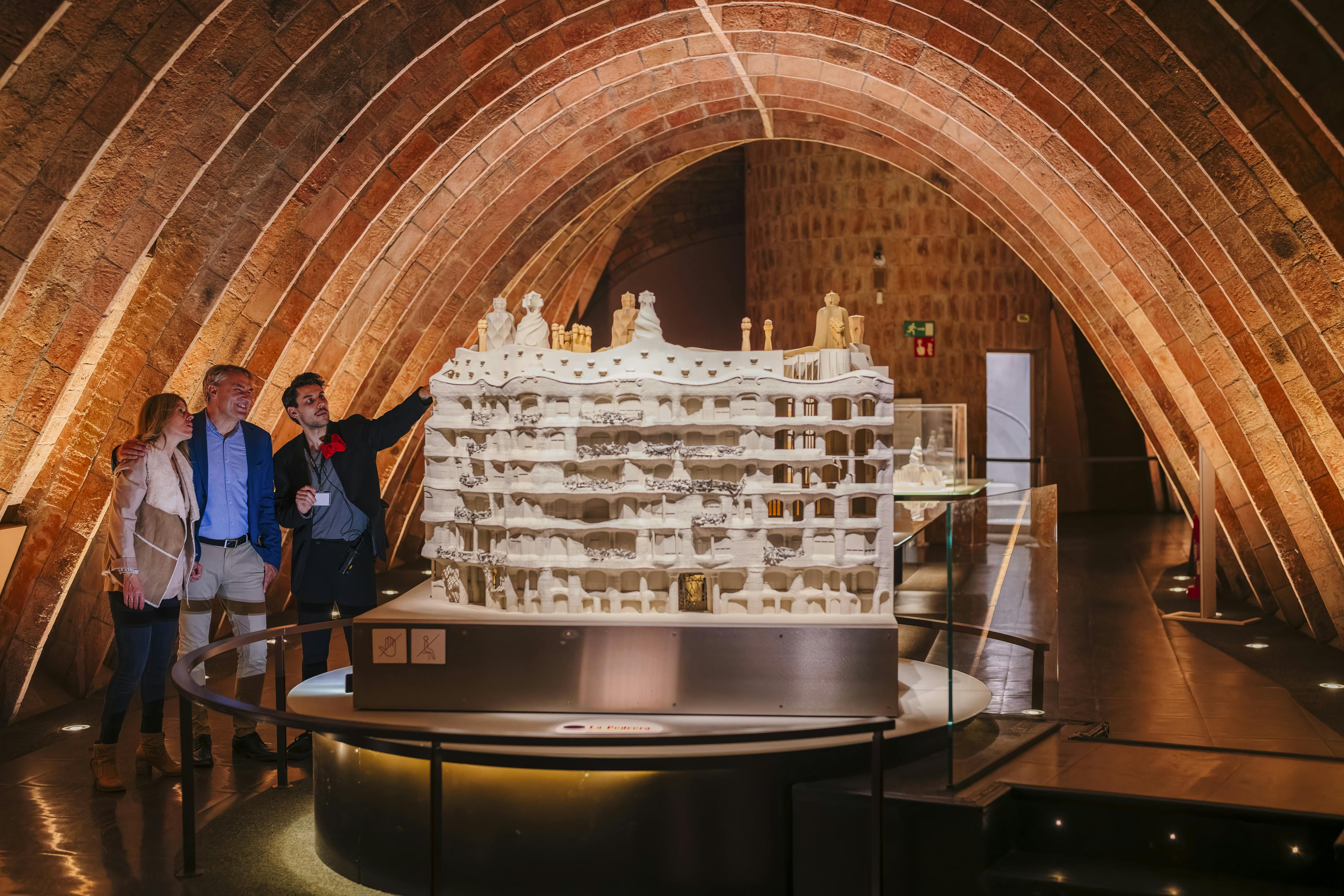 Tre persone osservano un modello dettagliato di un grande edificio sotto un soffitto ad arco in mattoni con un'illuminazione calda.
