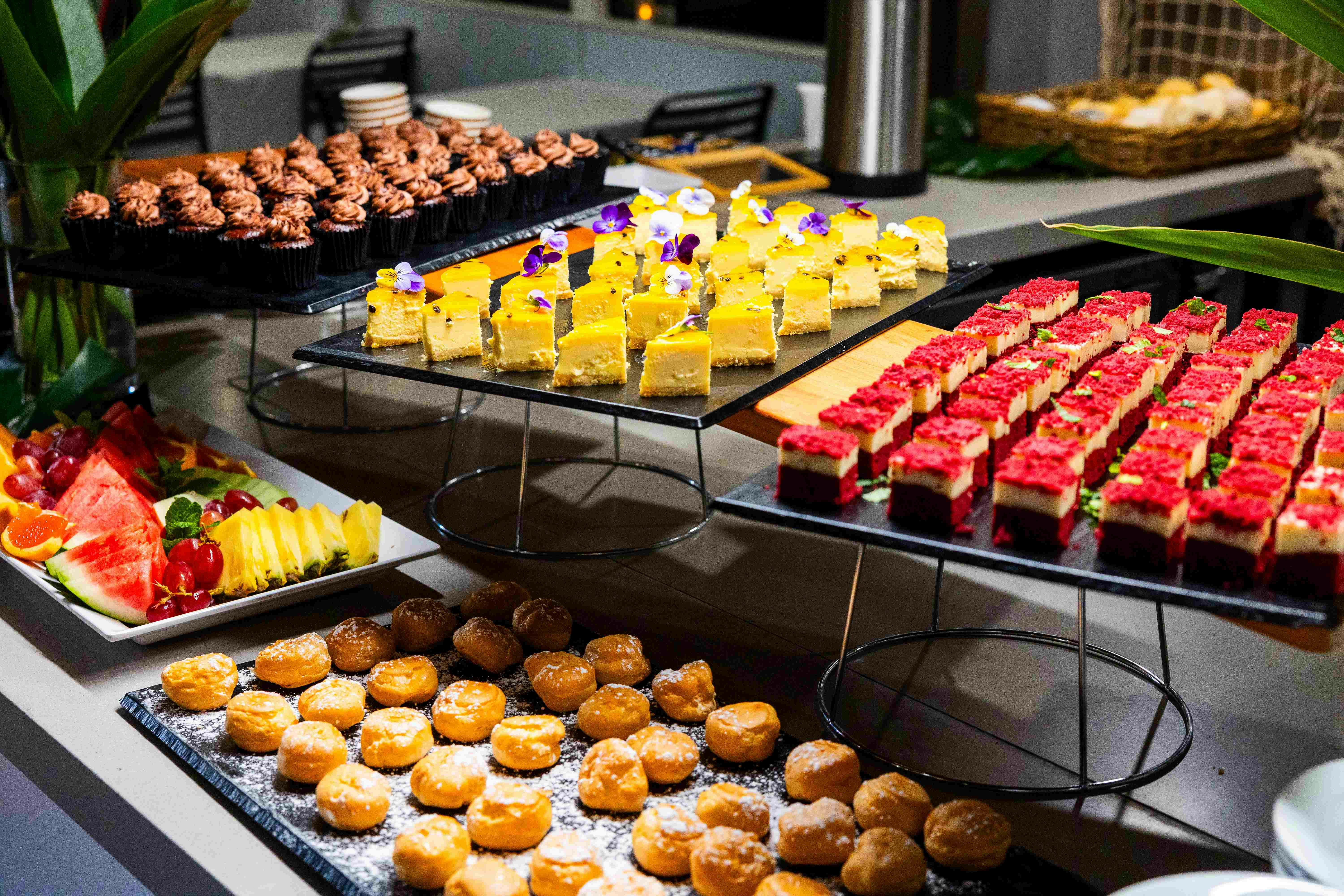 托盘上的各种甜点，包括巧克力纸杯蛋糕、带花的黄色蛋糕、红顶酒吧和粉状甜甜圈孔。