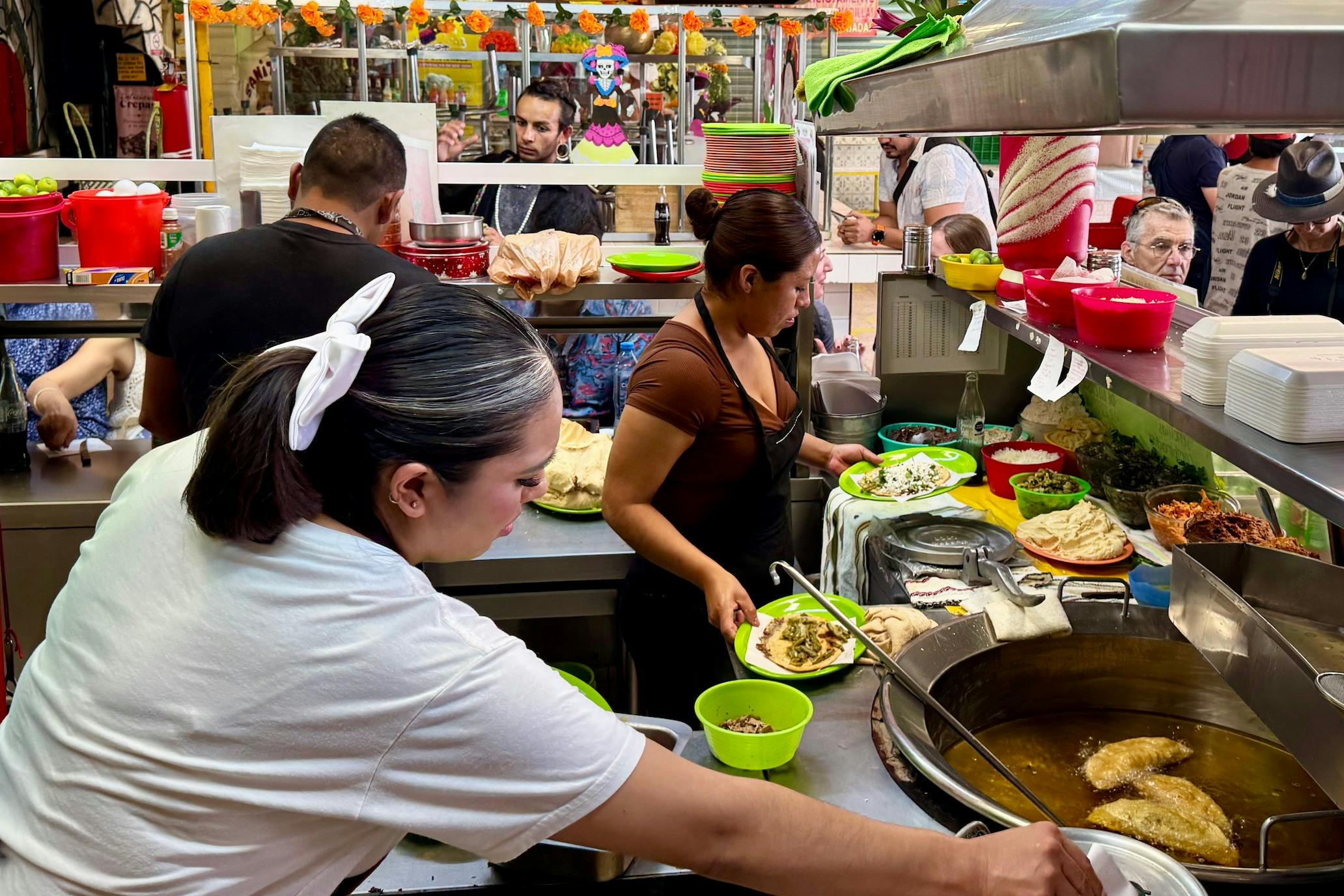 Menschen, die in einer geschäftigen Küche mit verschiedenen Gerichten und Zutaten auf den Theken in einer lebhaften Umgebung Essen zubereiten und servieren.