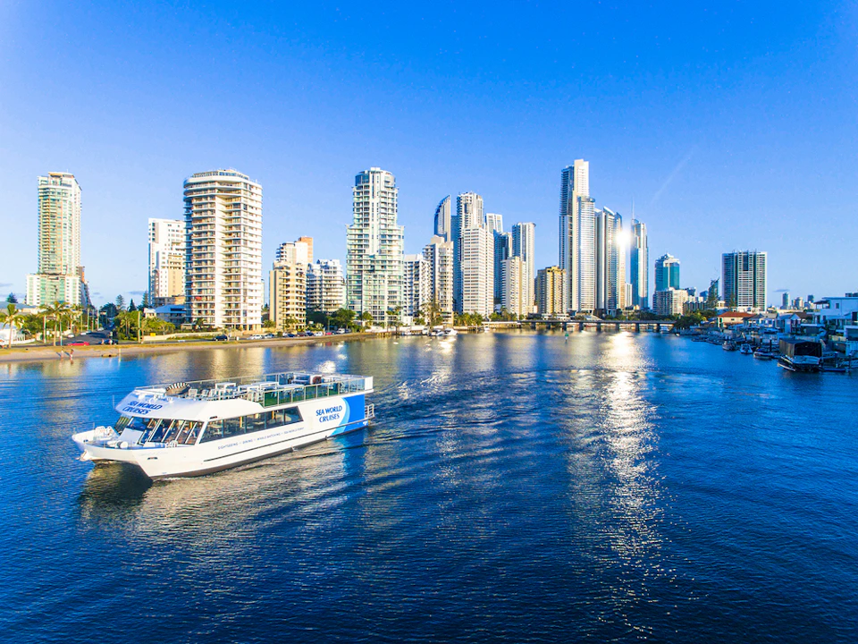 Boat on a river with modern, tall buildings in the background under a clear blue sky.