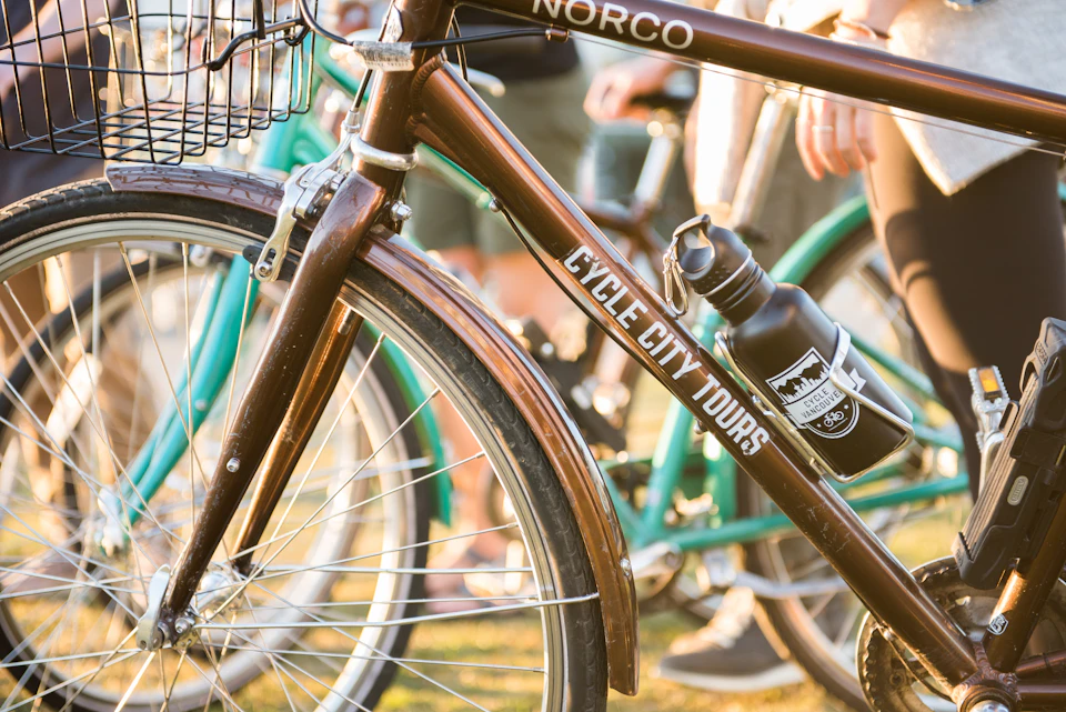 Close-up of bicycles with "Cycle City Tours" sign and water bottles attached to frames. Several people are visible in the background.