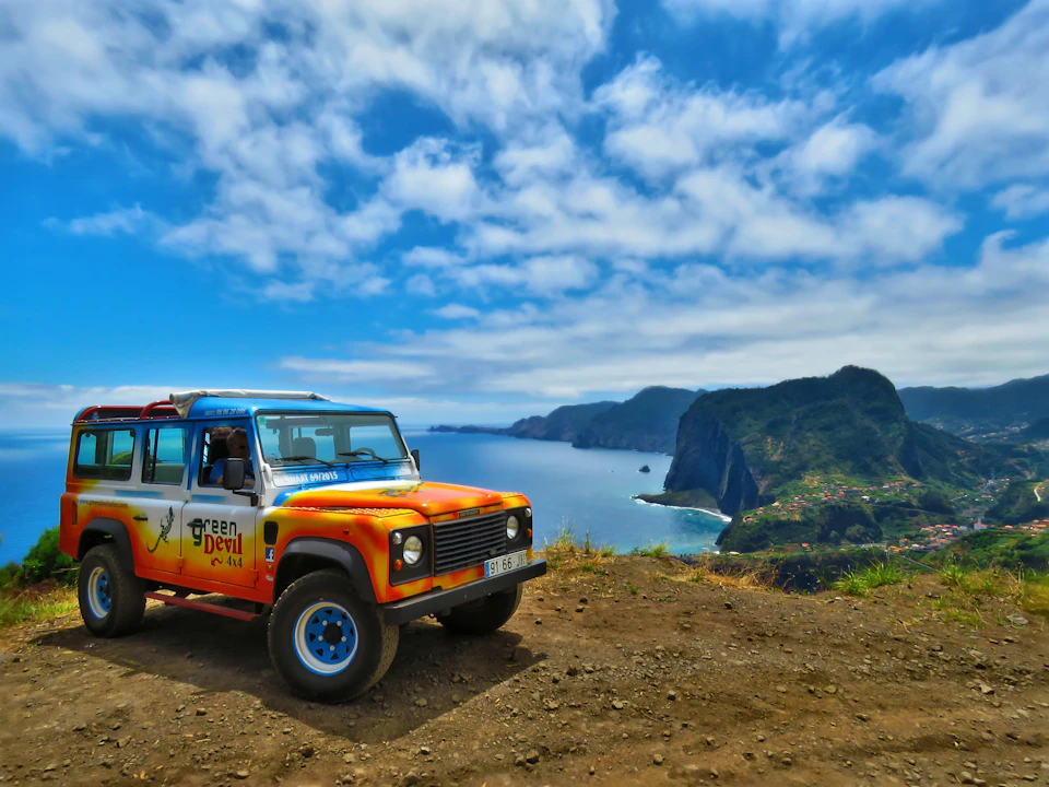 A colorful 4x4 vehicle parked on a cliff overlooking a scenic coastal landscape with blue skies and rugged cliffs in the background.