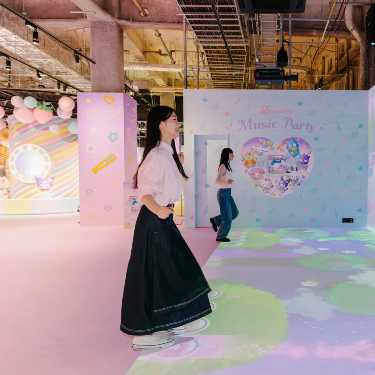 Two people walking inside a colorful, pastel-themed event space with decorative walls and soft lighting.
