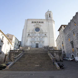 A grand staircase leading up to an ornate, historic cathedral flanked by old stone buildings under a clear blue sky.
