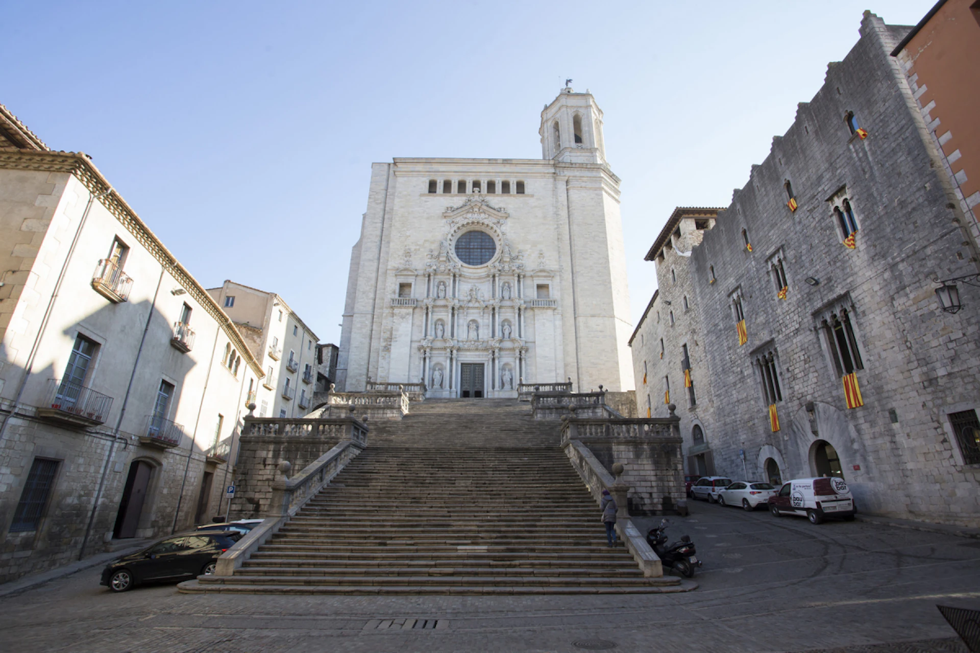 A grand staircase leading up to an ornate, historic cathedral flanked by old stone buildings under a clear blue sky.