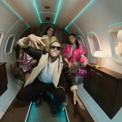 Tre personer som bär snygga kläder poserar i en privat jet med omgivande belysning, lampor och träskåp.