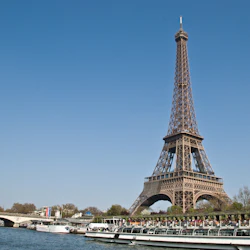 Eiffeltornet med en klarblå bakgrund, en bro och båtar på floden i förgrunden.