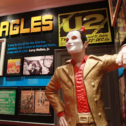 Museivisning med memorabilia inklusive stor "McGonagles" -skylt, U2-affisch, svartvita foton och en staty av en man i guldkostym.