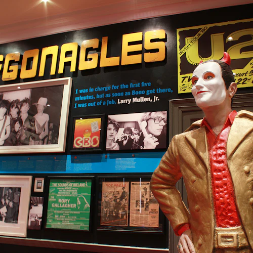 Museum display with memorabilia including large "McGonagles" sign, U2 poster, black-and-white photos, and a statue of a man in a gold suit.