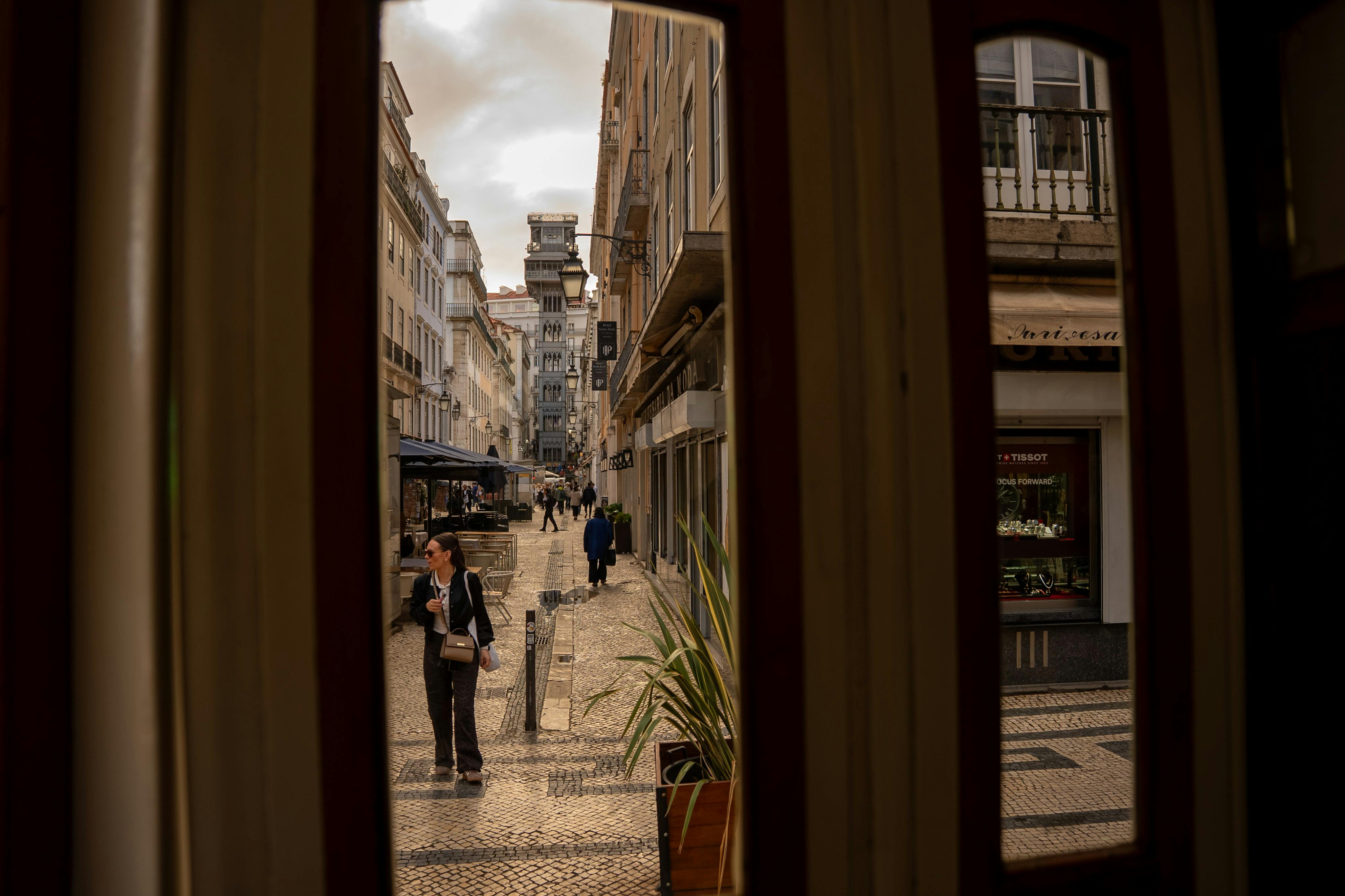 창문으로 둘러싸인 보행자, 상점, 유서 깊은 엘리베이터를 배경으로 좁은 거리가 한눈에 들어옵니다.