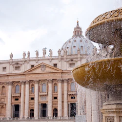 The image shows St. Peter's Basilica's dome and facade in Vatican City, with a stone fountain in the foreground.