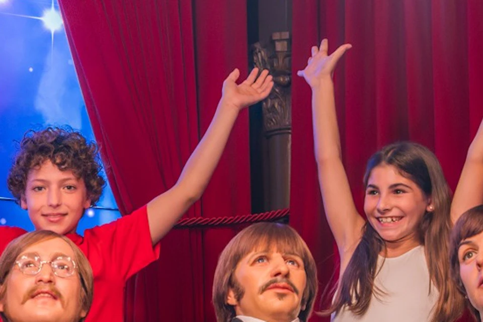 A group of people posing with wax figures on a couch under stage lighting and red curtains, with a starry background.