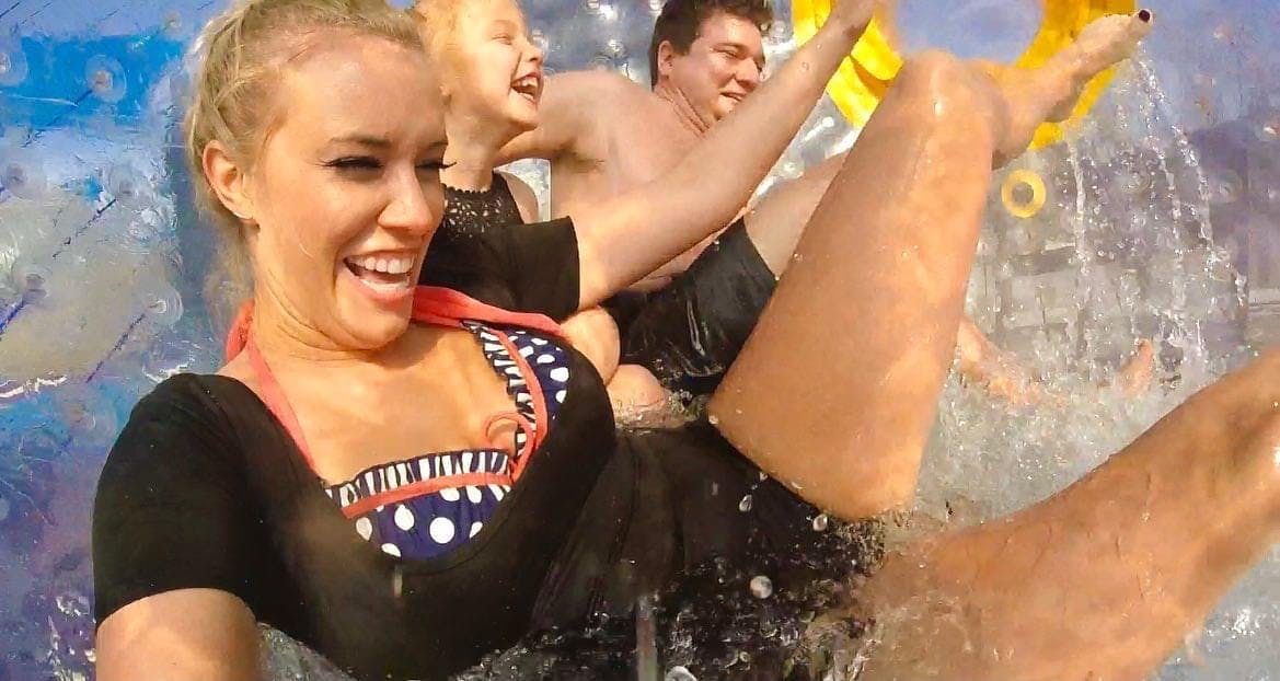 Tre persone sorridono e ridono mentre scivolano lungo una giostra acquatica, schizzando l'acqua intorno a loro.