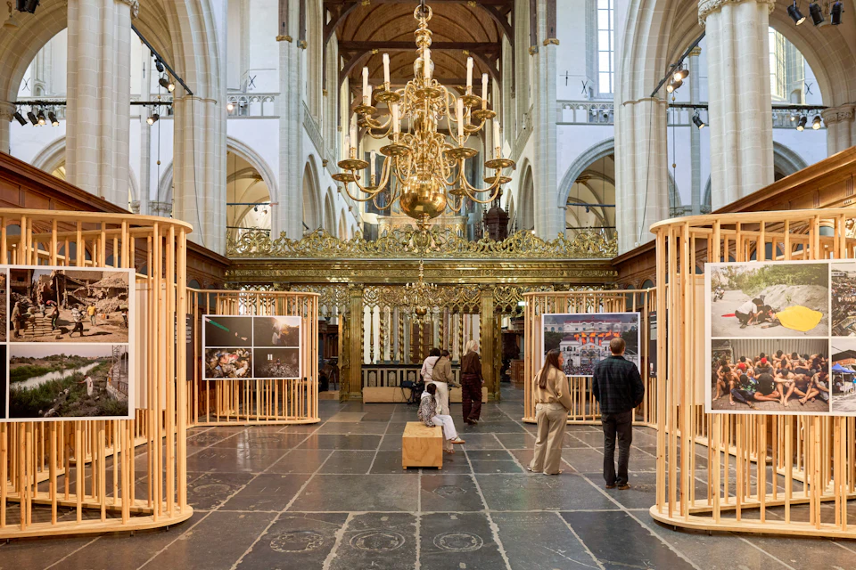 The interior of a church with an exhibition display featuring photographs on show. A golden chandelier hangs above visitors viewing the exhibits.