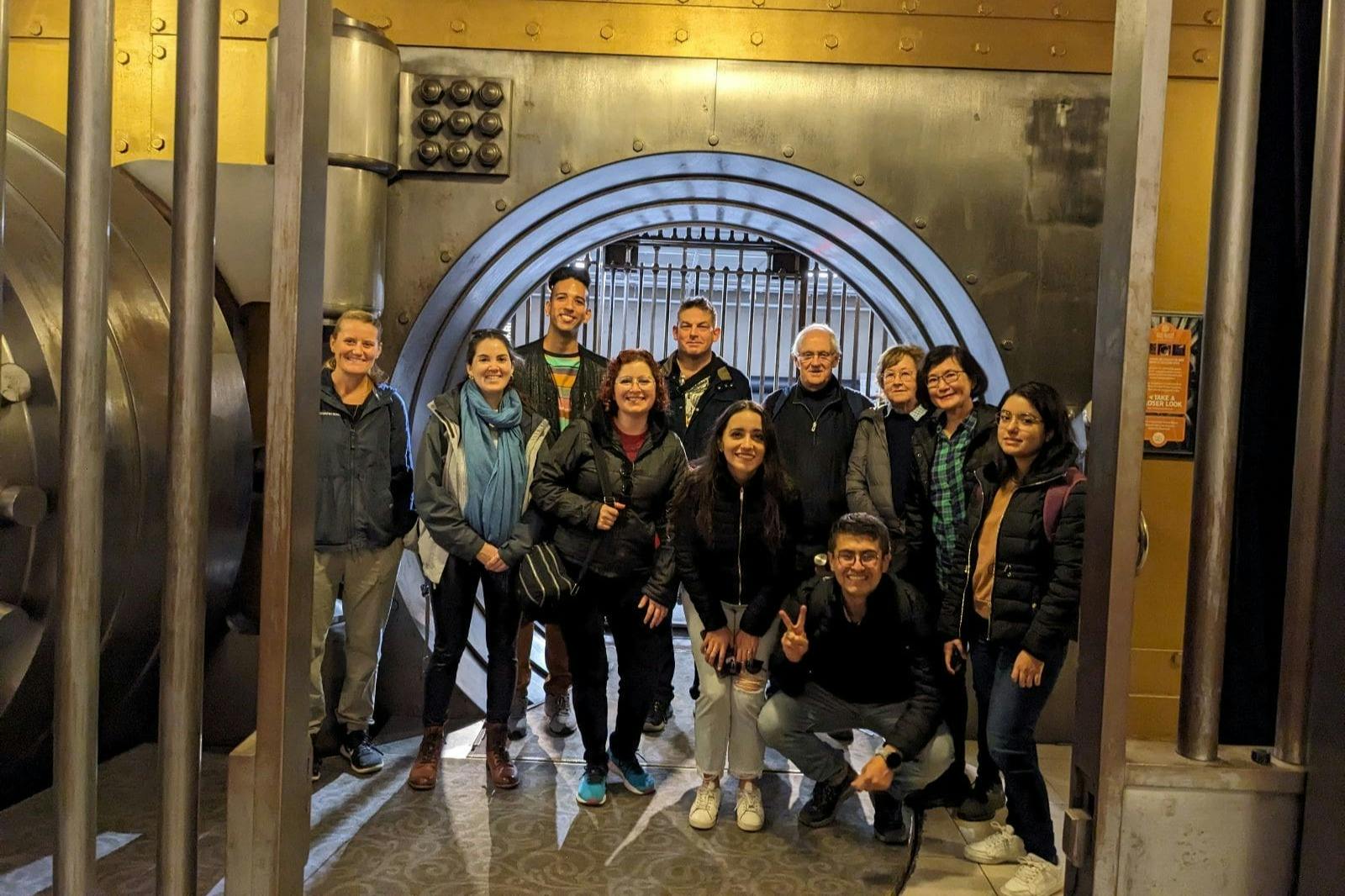 一群人在一扇大型圆形金属金库门前摆姿势，处于室内环境。