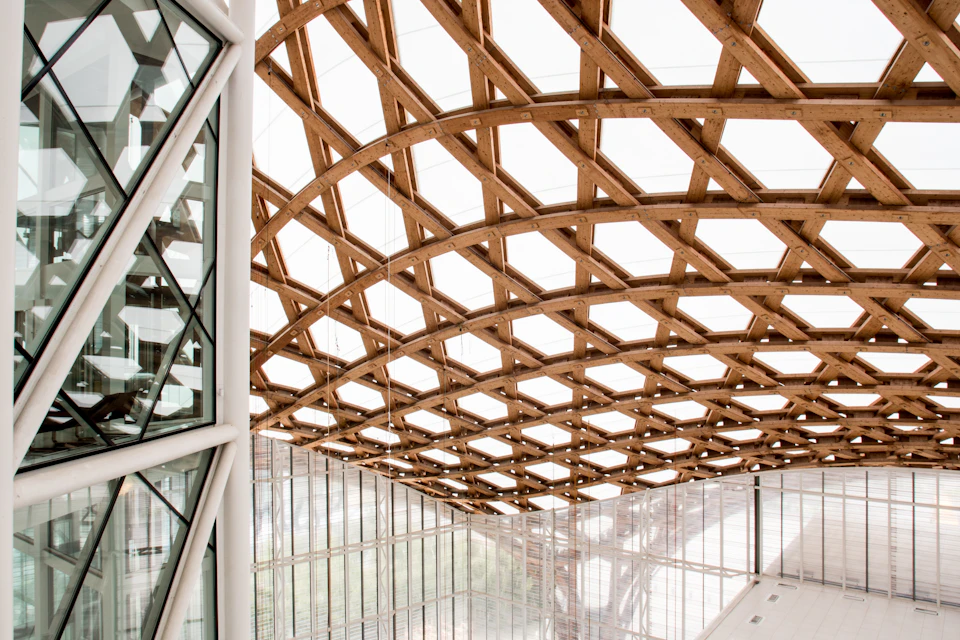 Modern building interior with a large wooden lattice ceiling structure and glass walls.