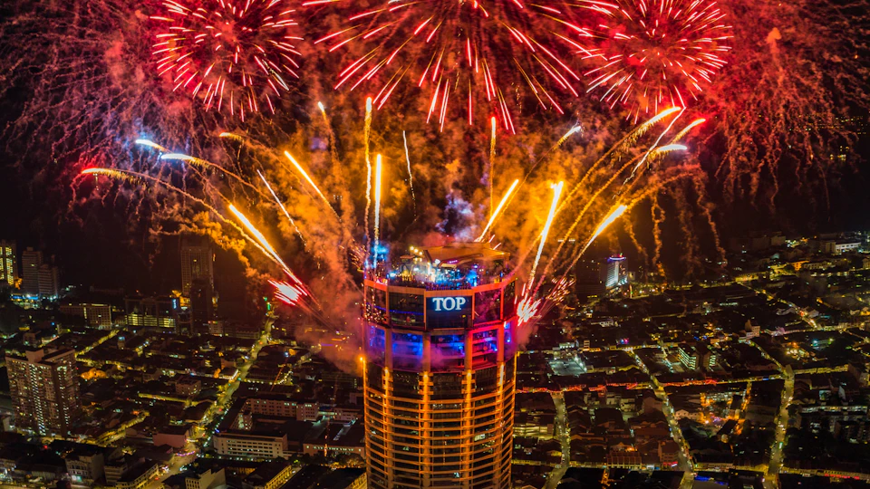 A tall building with a circular top, labeled 'TOP,' surrounded by vibrant fireworks in a cityscape at night.