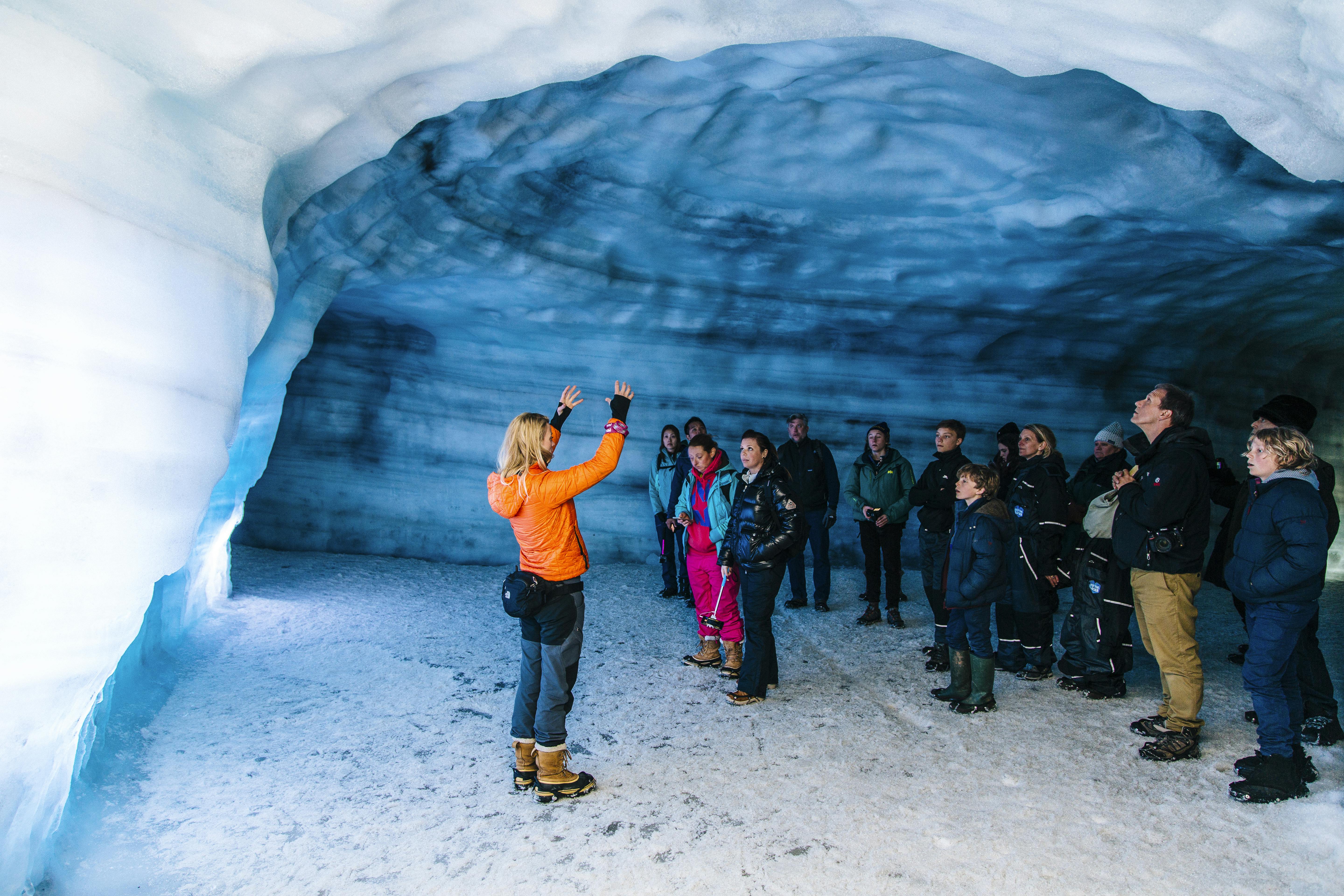 Ein Tour Guide spricht zu einer Gruppe von Menschen in einer Eishöhle, die von eisigen Wänden und einem gefrorenen Boden umgeben ist.
