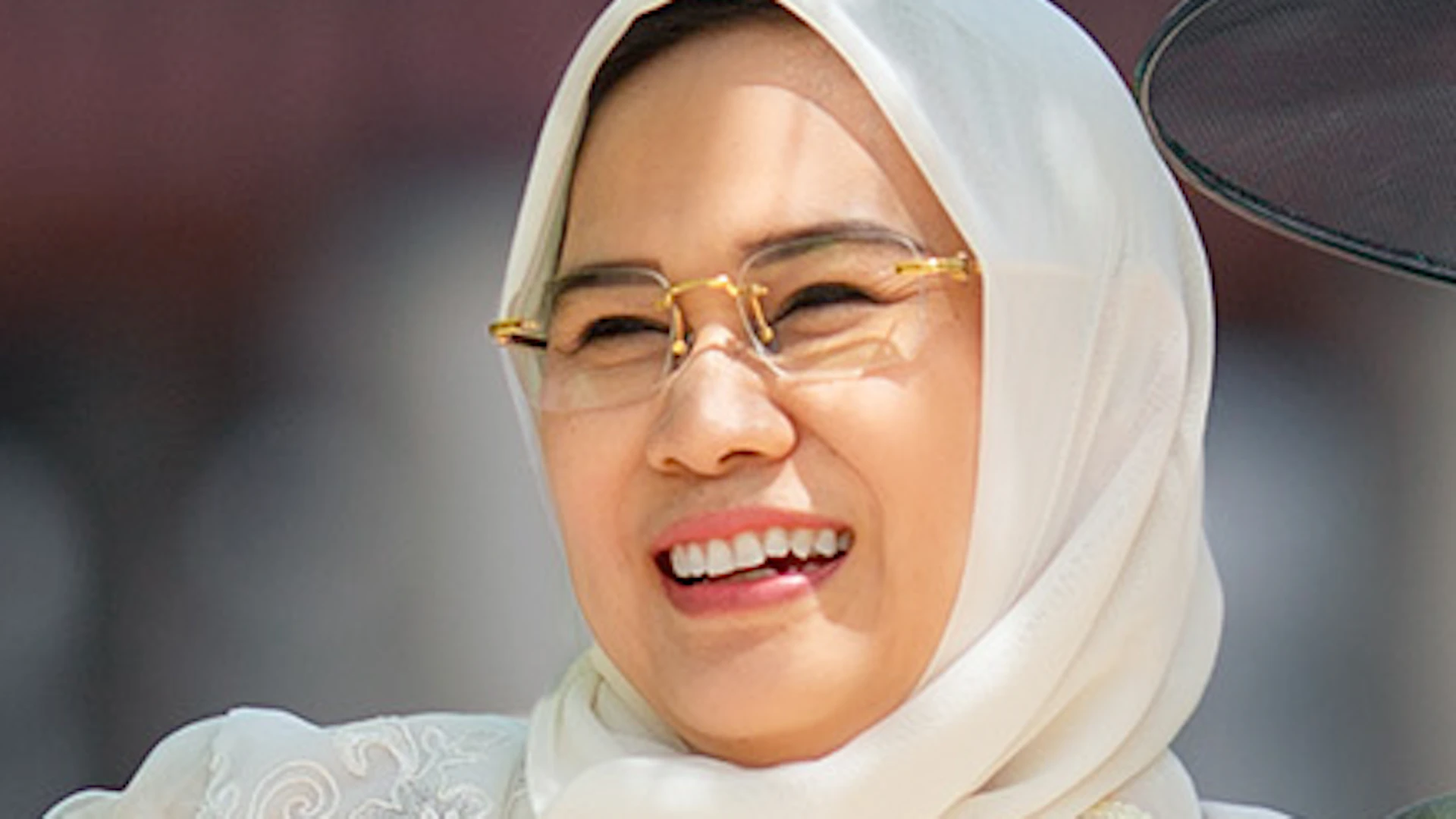 Three people wearing traditional clothing, smiling and interacting outdoors in a bright, sunny setting.