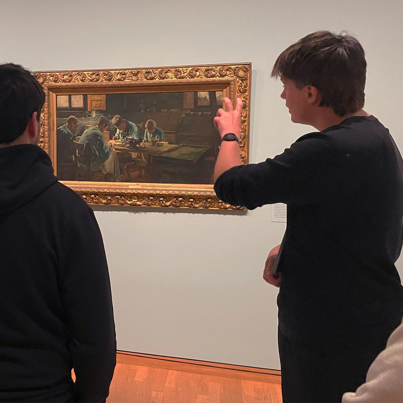 People observing a framed painting in a museum setting, with one person gesturing during a discussion.