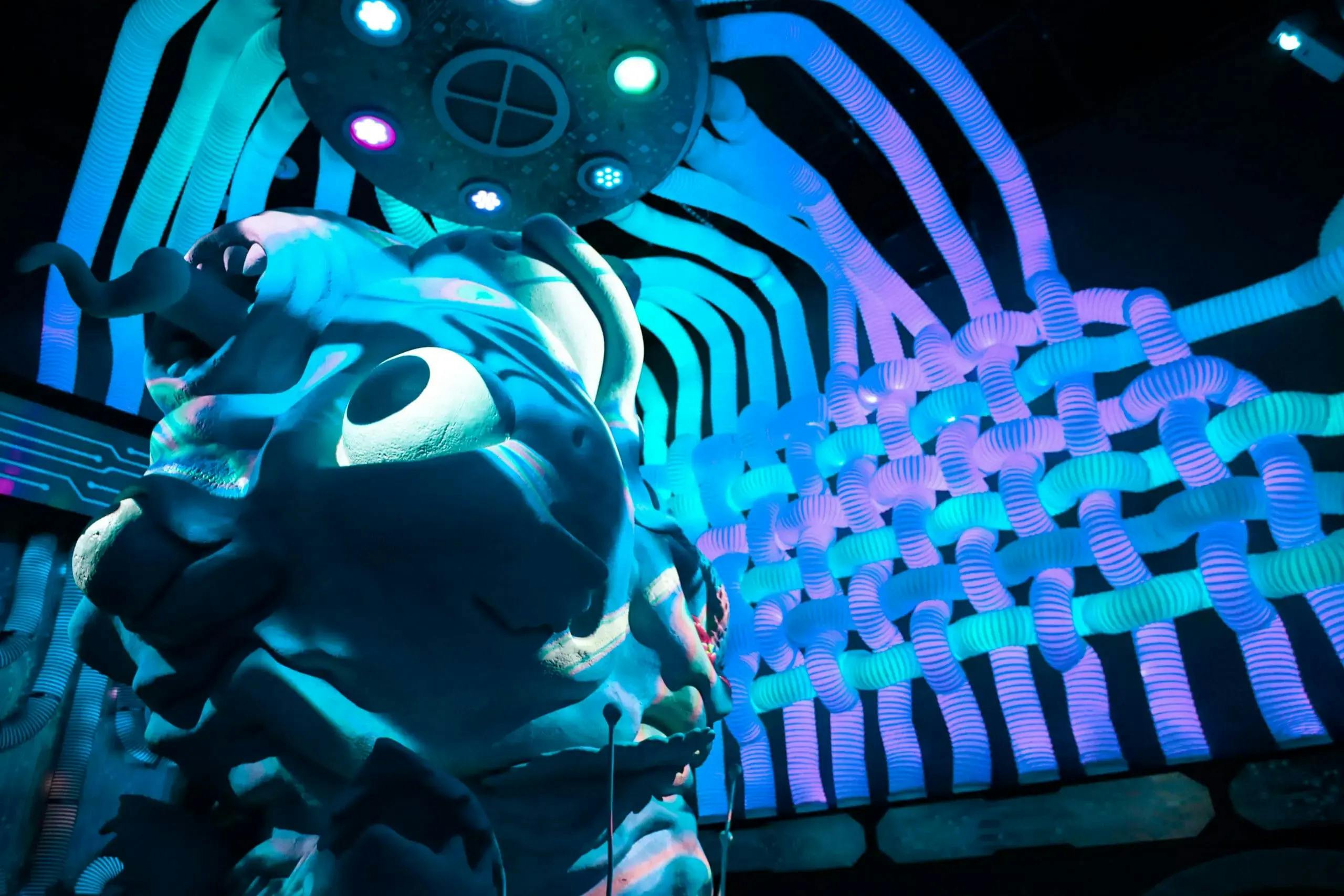 Large, colorful, abstract sculpture with light patterns and tubes creating a surreal, futuristic atmosphere.