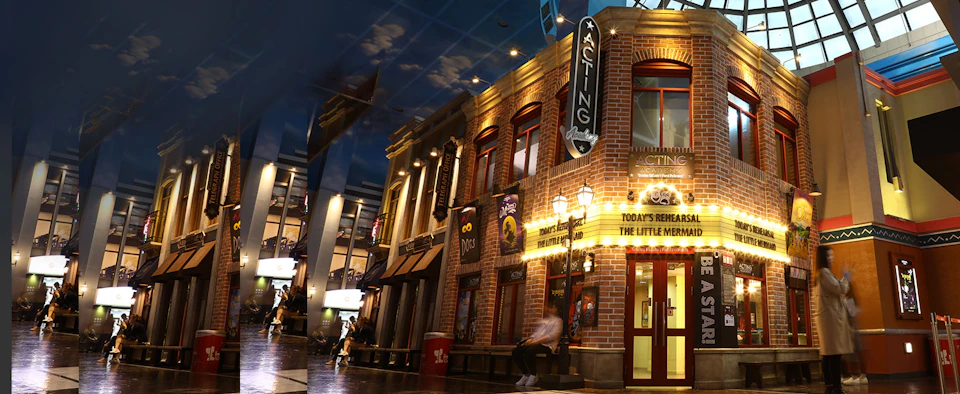 An indoor street scene with a brick building displaying signs for an acting academy, lit by warm yellow lights at night.