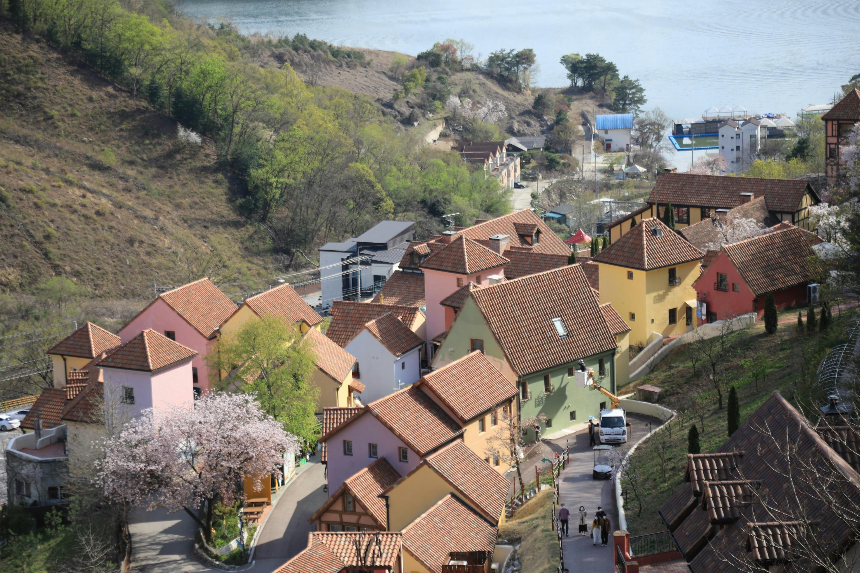 A hillside village with colorful buildings, red-tiled roofs, and a view of a river surrounded by trees and hills.