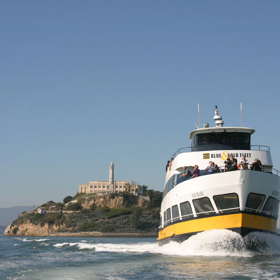 A ferry labeled "Blue & Gold Fleet" on the water with Alcatraz Island and its buildings in the background.