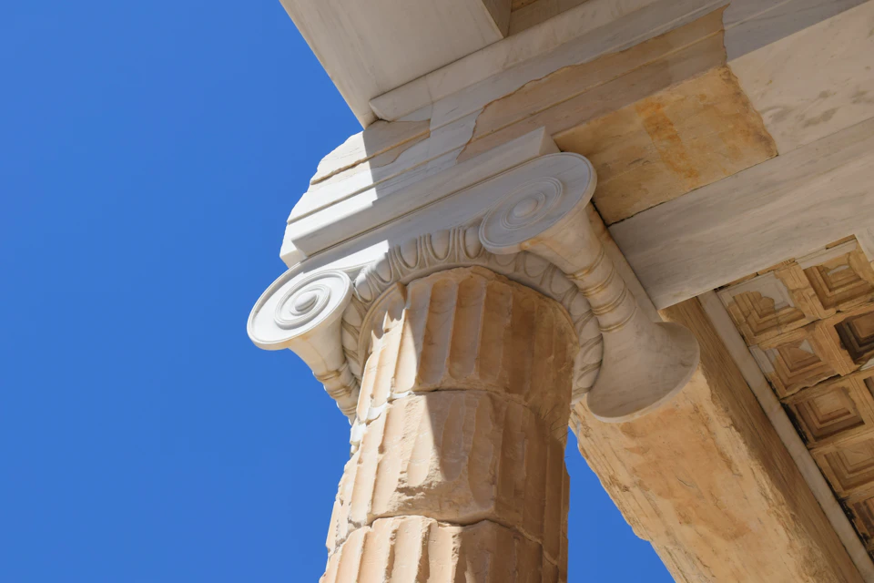 A close-up of an ancient Ionic column and entablature under a clear blue sky.