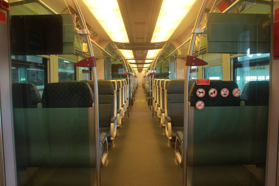 Interior view of a modern train car with rows of empty seats and a brightly lit ceiling.