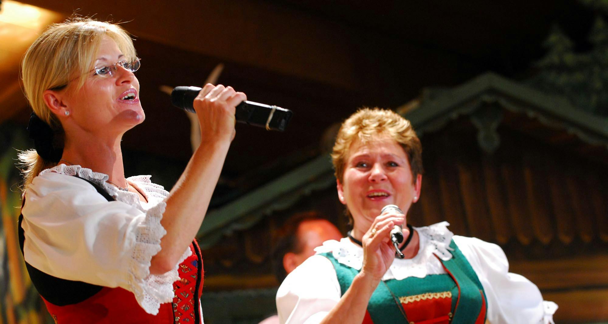 전통적인 복장을 한 두 여성이 무대에서 배경 요소가 흐릿한 마이크를 불렀습니다.