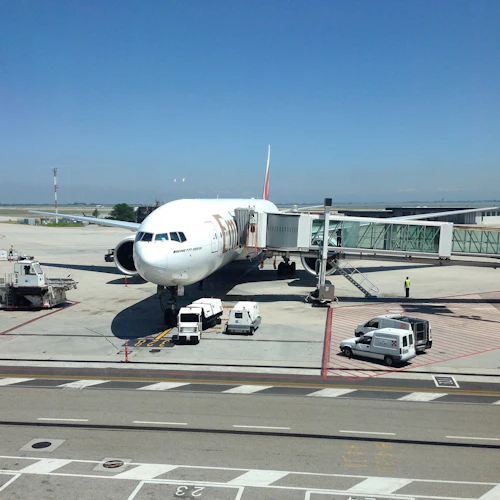 Ett flygplan är dockat vid en flygplatsgrind med jetbroar bifogade; servicefordon och personal finns på asfalten.