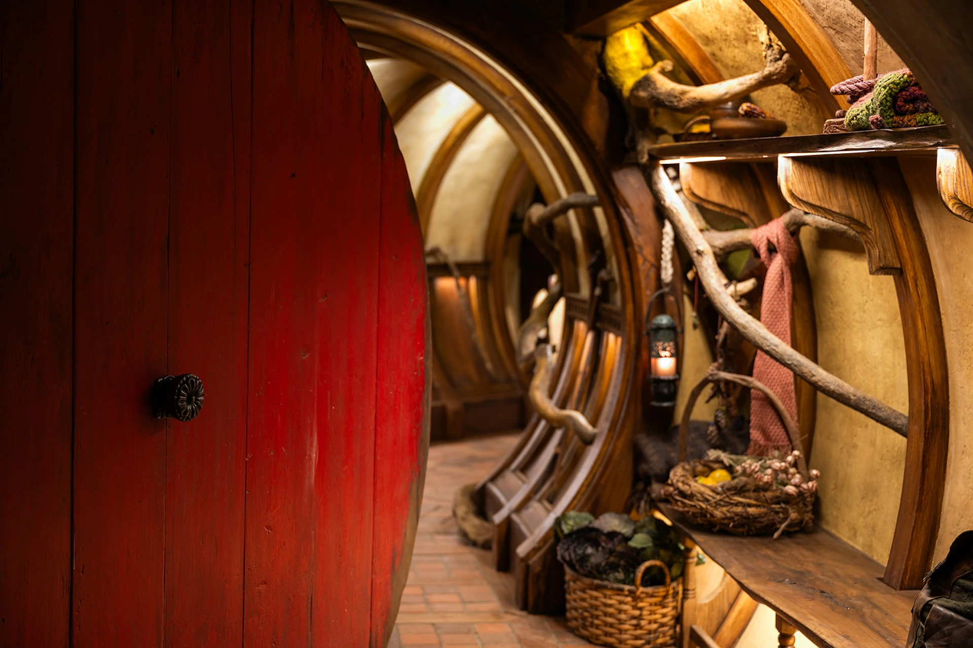 A cozy, curved interior with wooden and natural decor, a red door, a wicker basket, and a lantern on a shelf.