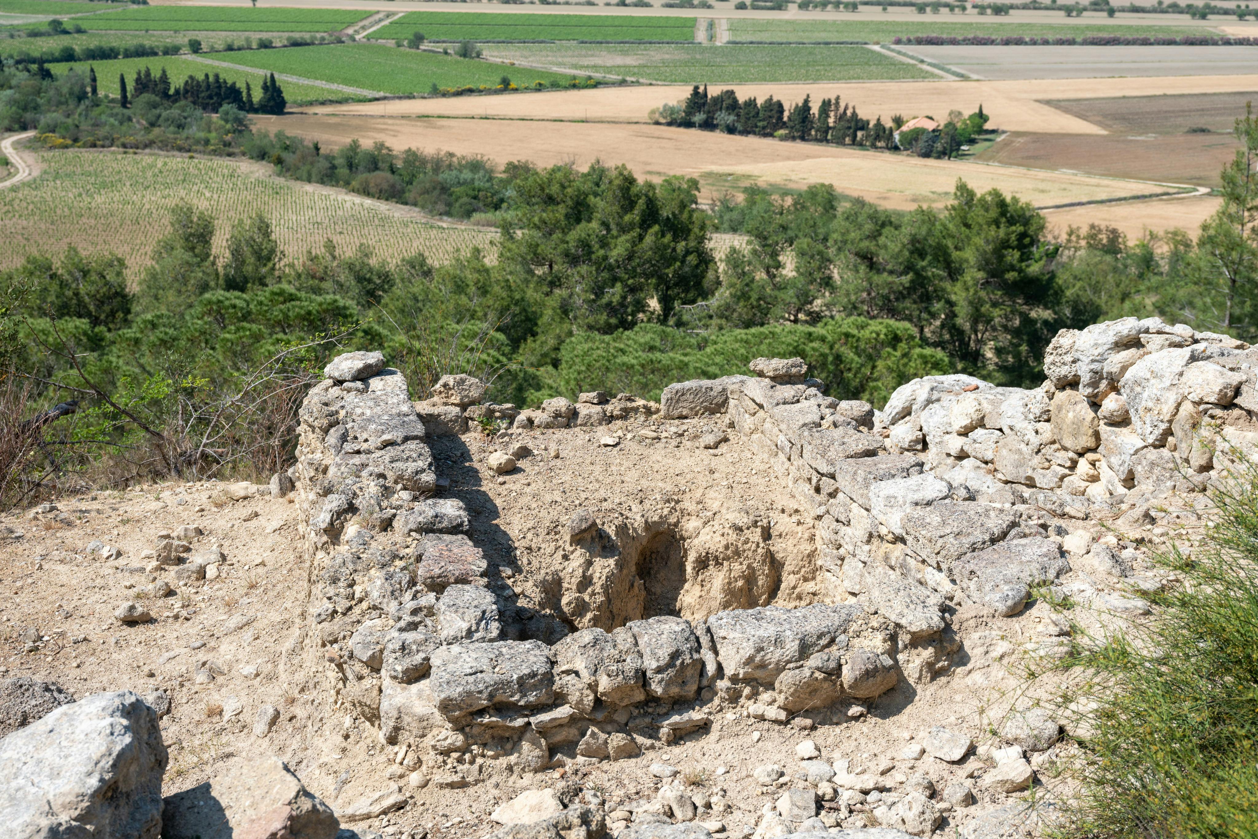 Ruines en pierre sur une colline surplombant les champs et les arbres sous un ciel clair.